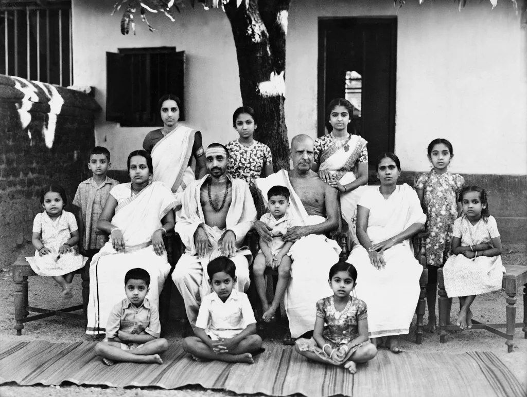Swami Chinmayananda seated with children and families in an archival group photograph