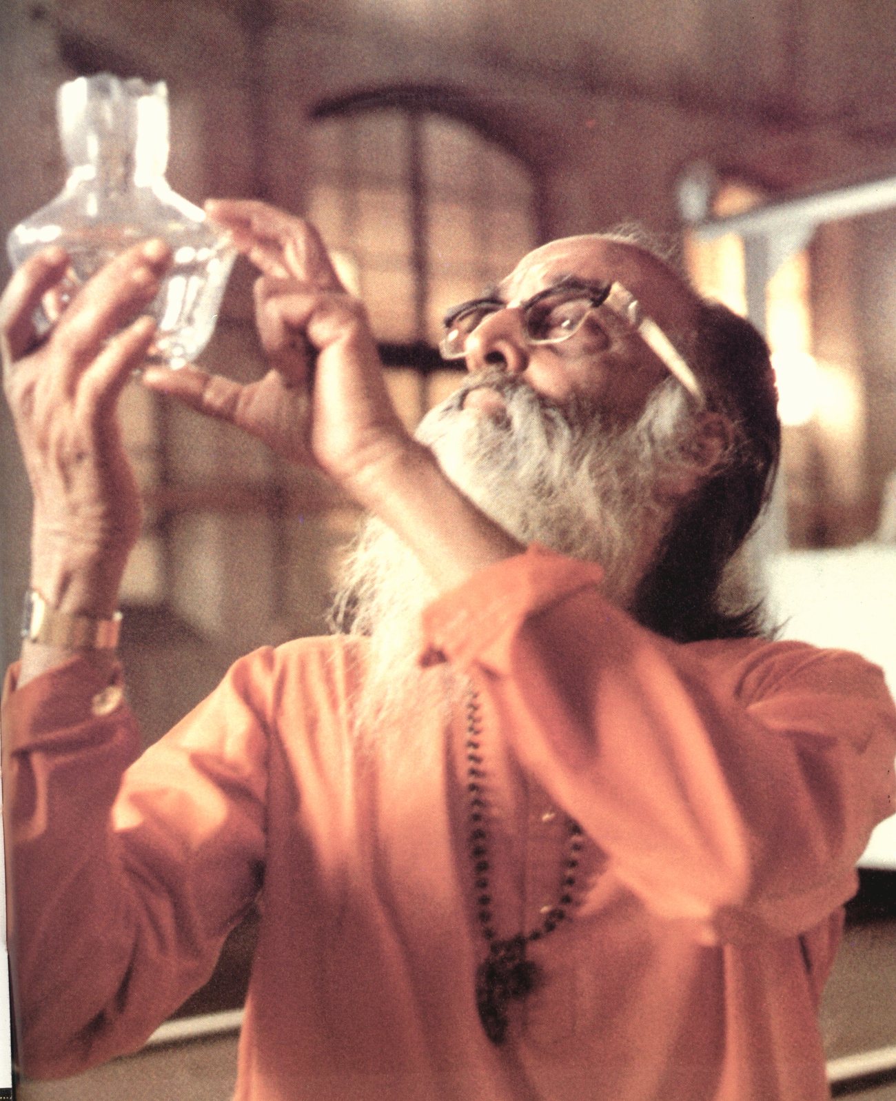 Pujya Gurudev Swami Chinmayananda holding a laboratory flask up to the light, examining it
