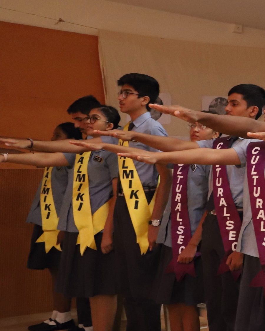 Students at a CIRS investiture ceremony wearing yellow Valmiki house sashes, right hands raised in the pledge