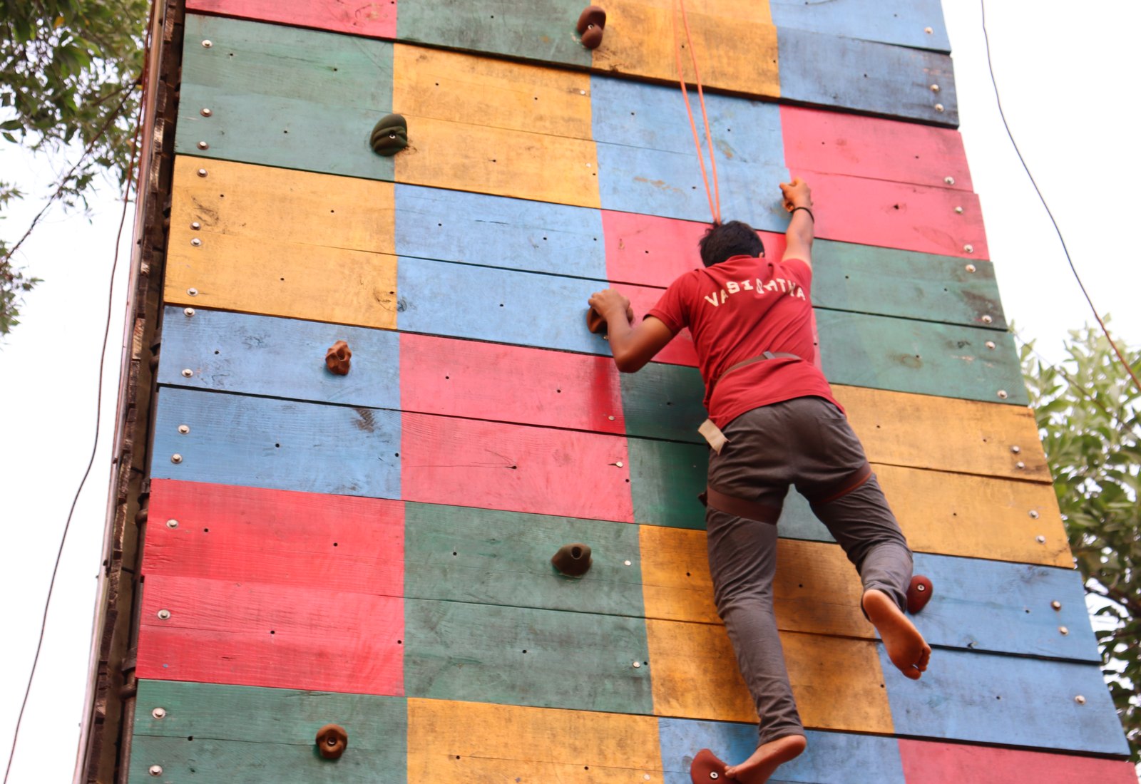 A Vasishta student climbing a wall, the house name visible on the red shirt