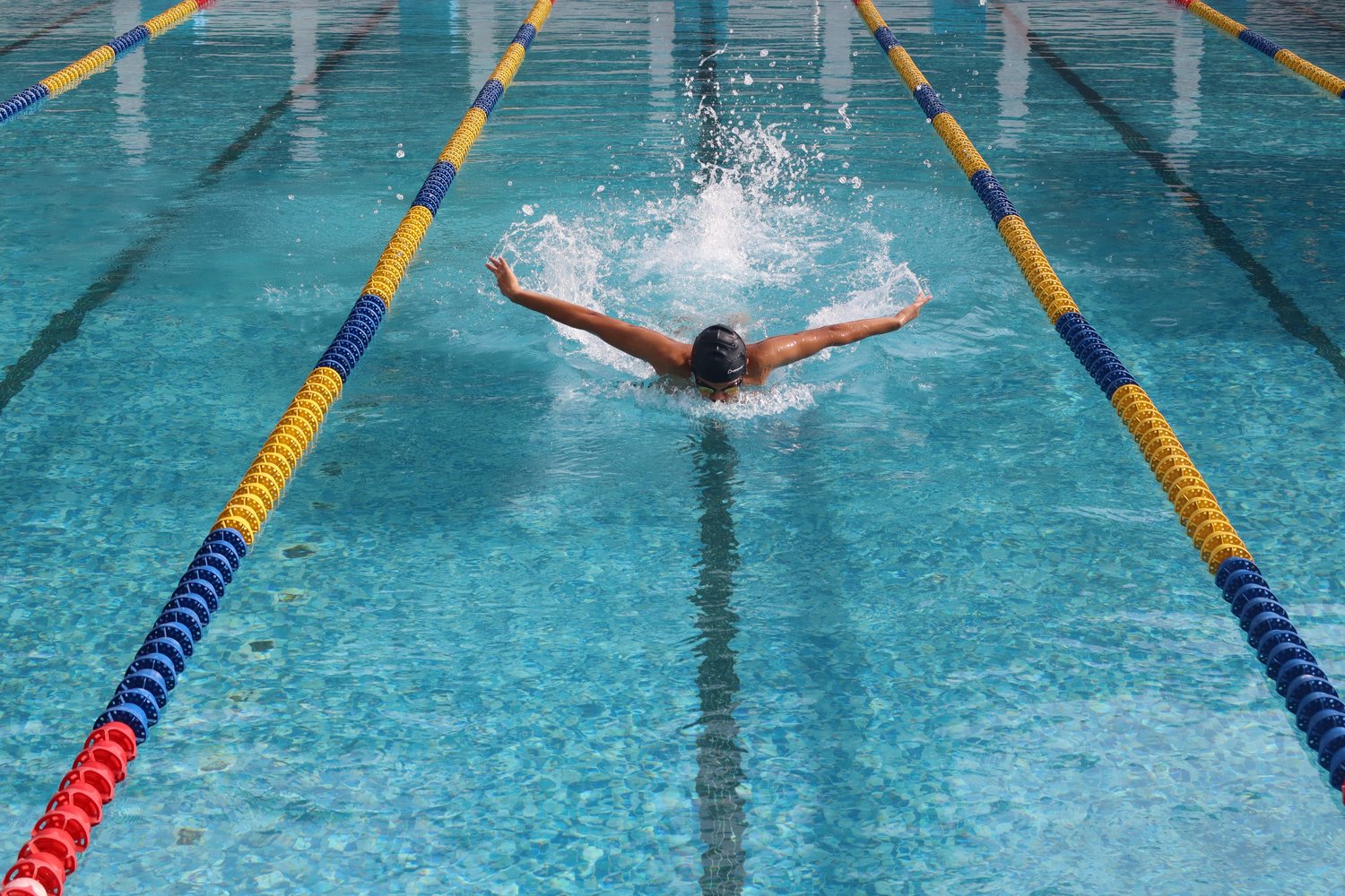 A swimmer mid-butterfly between two lane ropes in the outdoor pool.