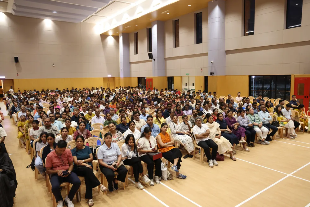 A wide view of a hall filled with parents, students and teachers seated on chairs and on the floor