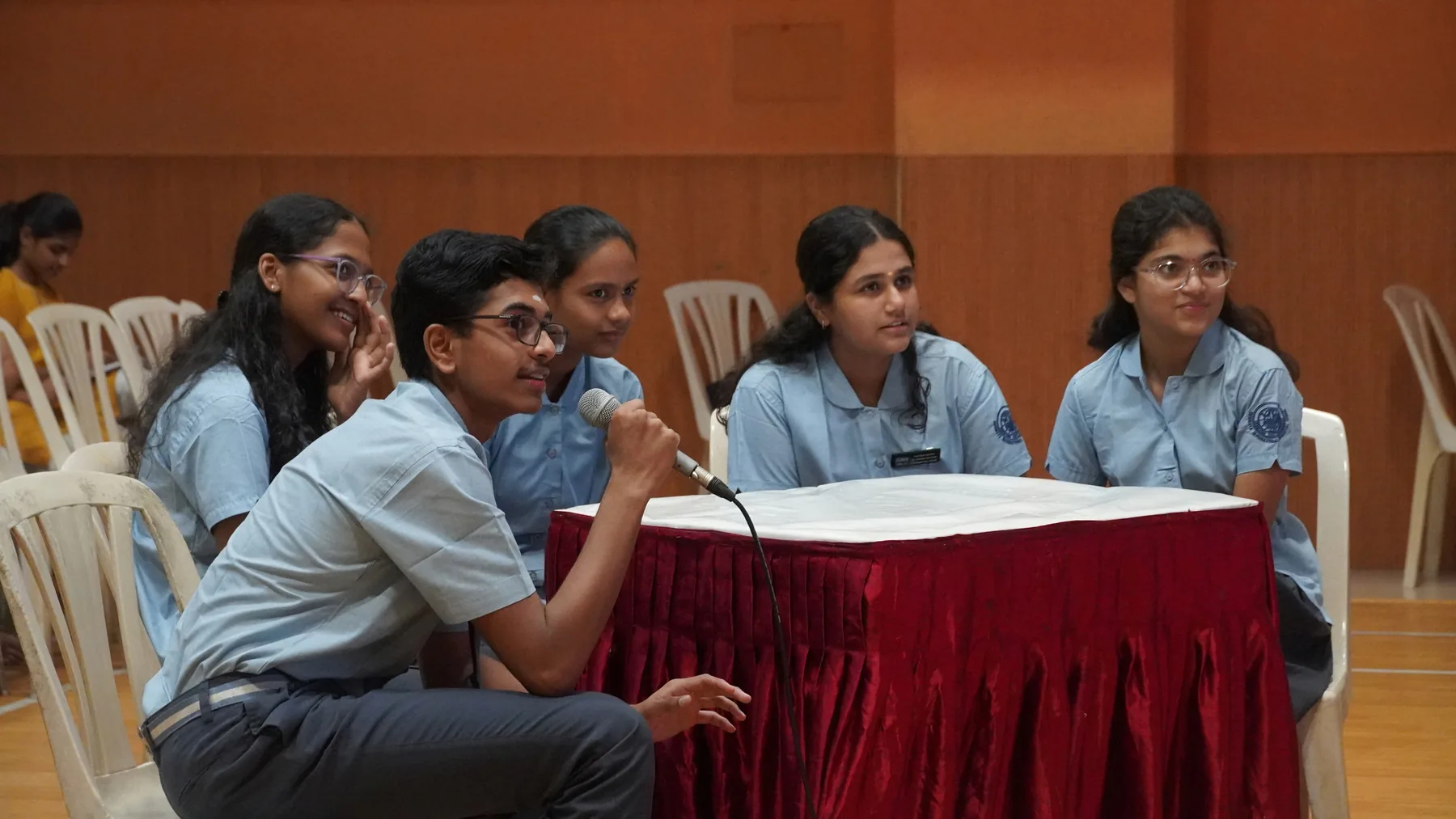 Students seated at a red-clothed table with microphones