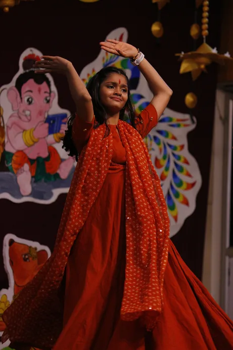 A girl in a red dress dancing with her arms raised in front of a festival backdrop