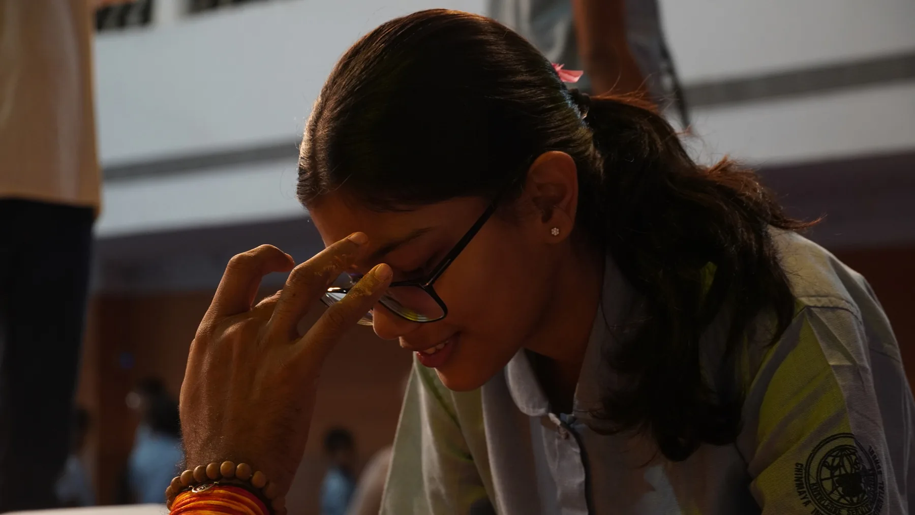 A student in glasses with her head bowed and her hand at her forehead
