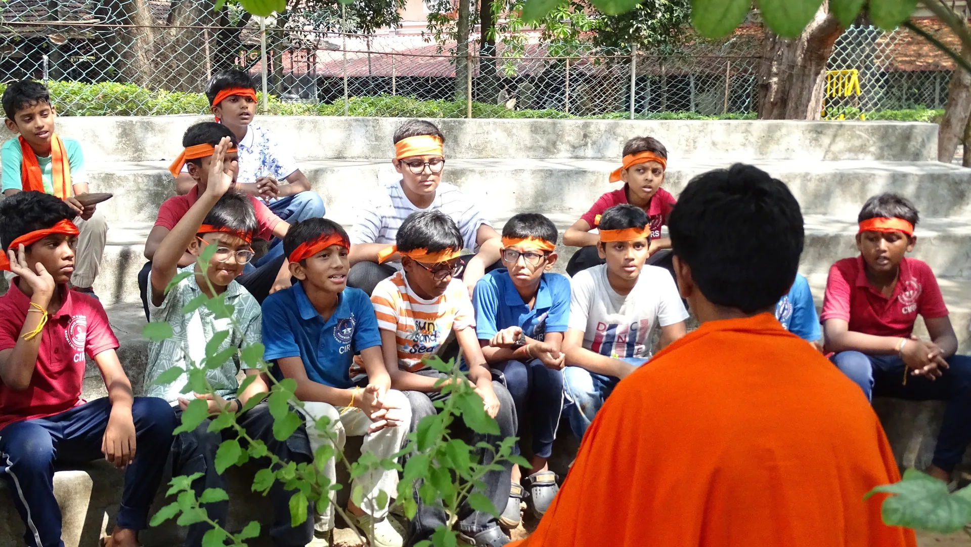 Students wearing coloured headbands seated on the amphitheatre steps, with a person in saffron in the foreground