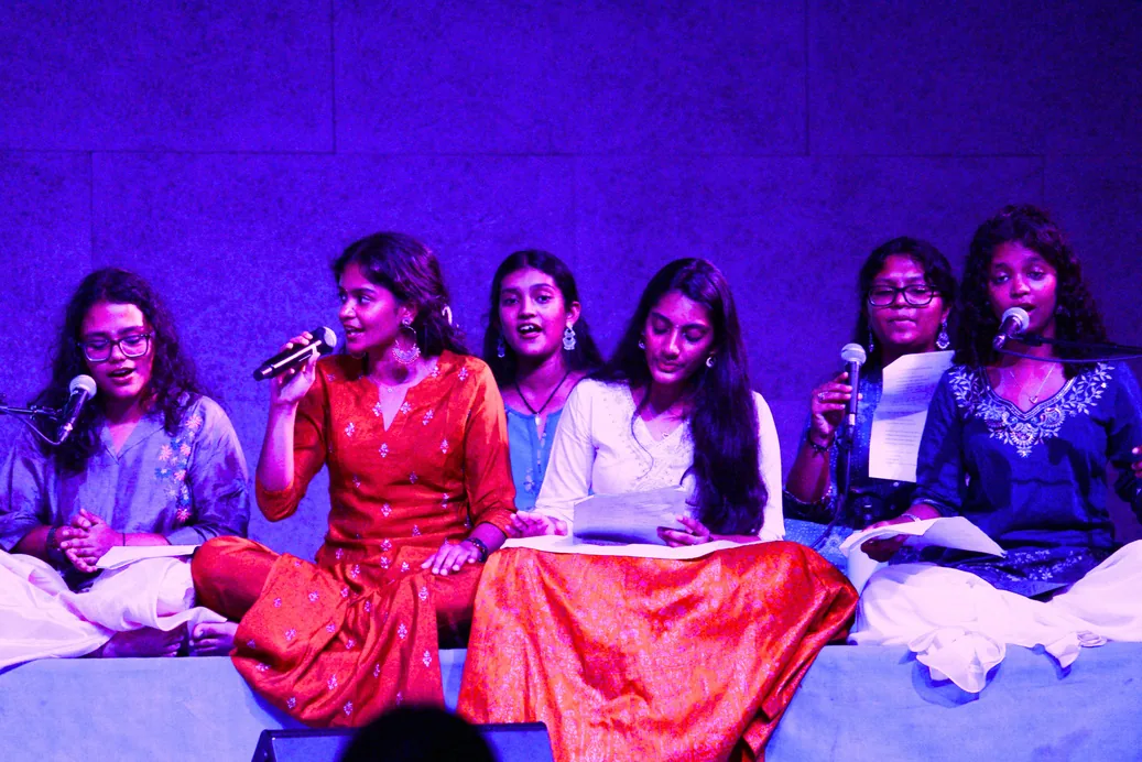 Students singing into microphones on a stage lit in blue