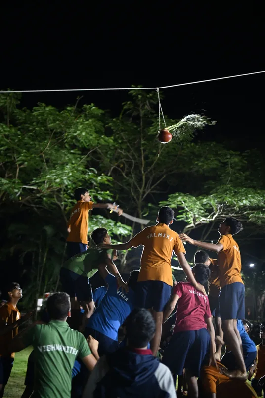 Students forming a human pyramid at night beneath a hanging pot