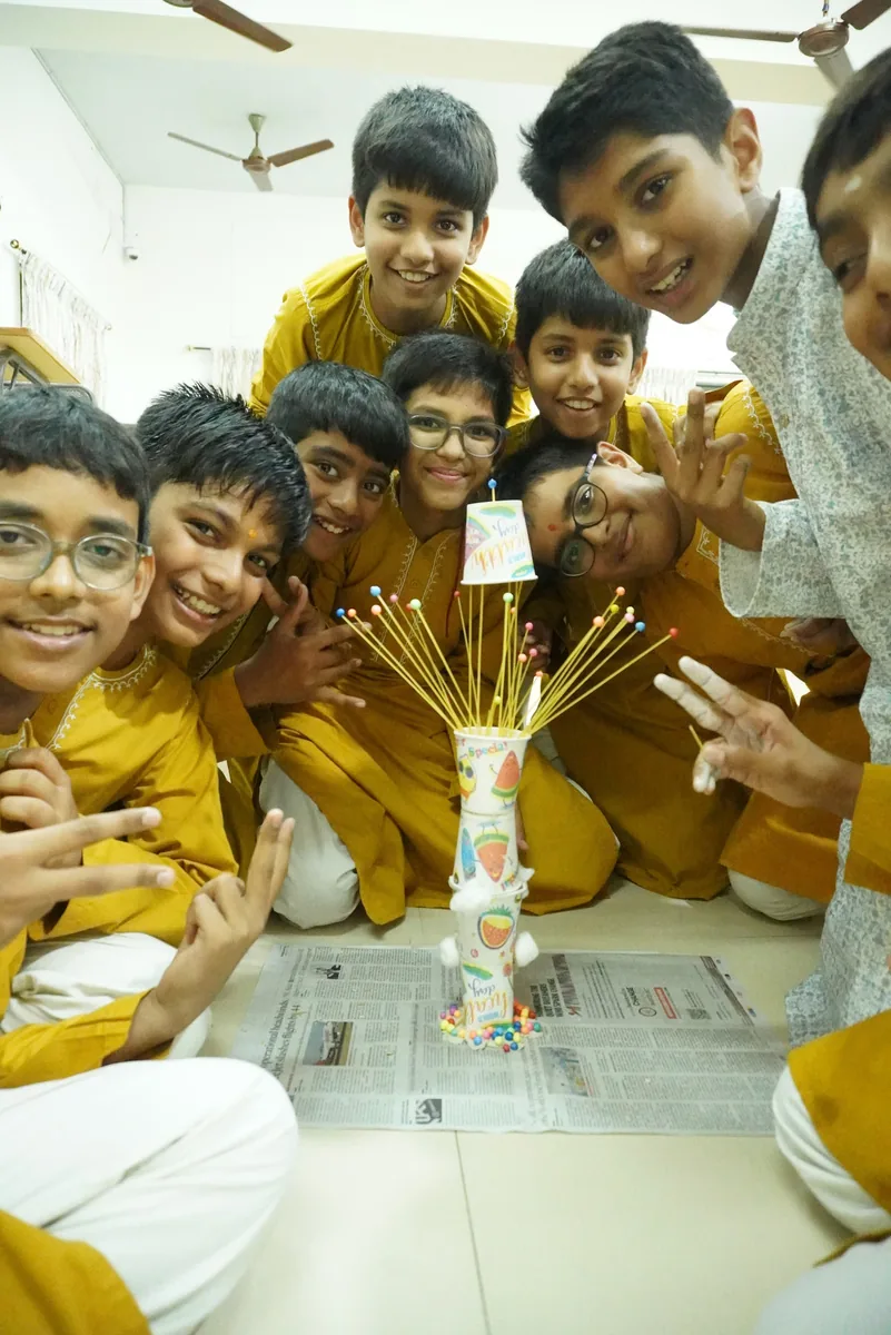 Students in mustard kurtas crowded around a tall tower of sticks