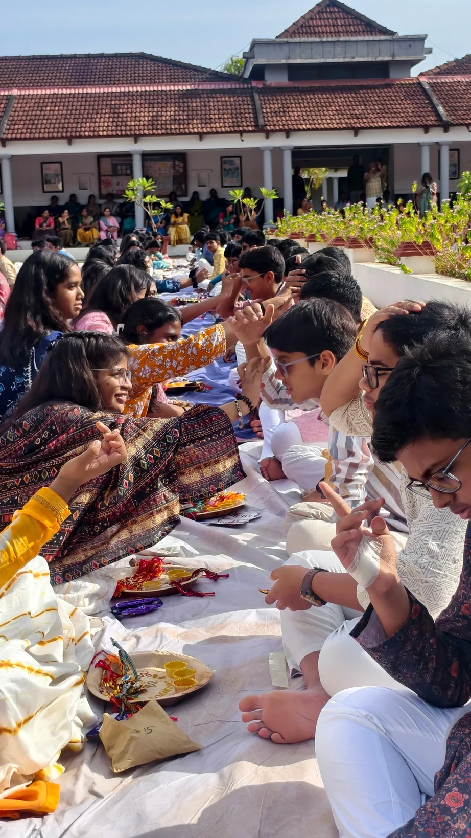 Students tying rakhis at a long table laid with plates