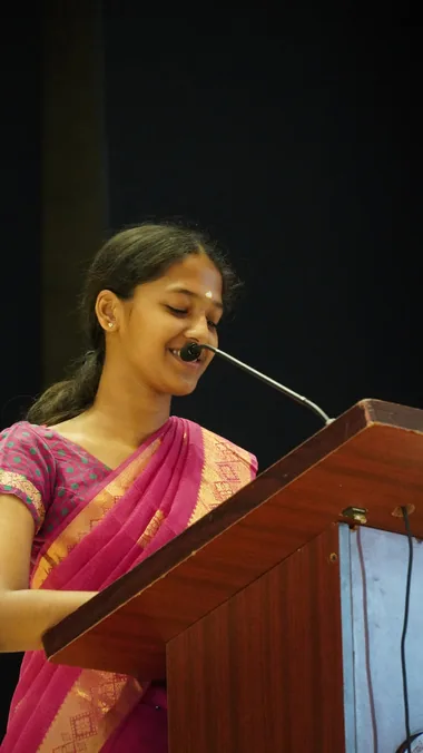 A girl in a pink sari speaking at a lectern