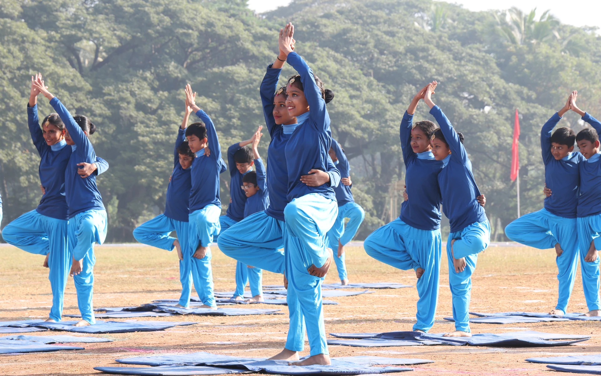 CIRS students in blue tracksuits holding a standing yoga pose on the school ground, hills behind them