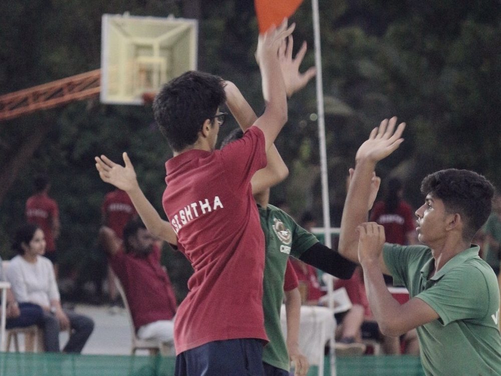 A shot going up towards the hoop, three players with their hands raised beneath it