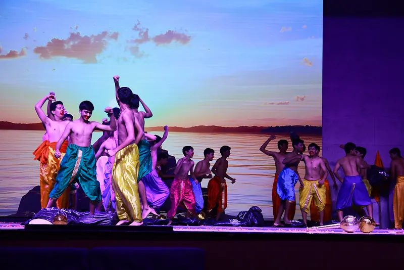 An ensemble in bright dhotis dancing before a sunset backdrop