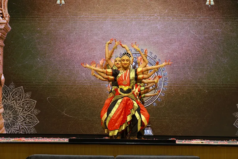 A dancer in red and gold at the centre of a many-armed tableau