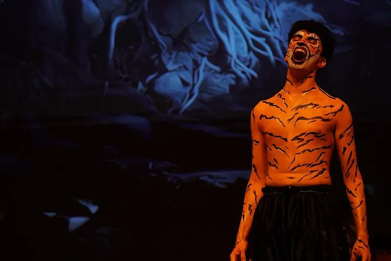 An actor in tiger body paint roaring, head thrown back