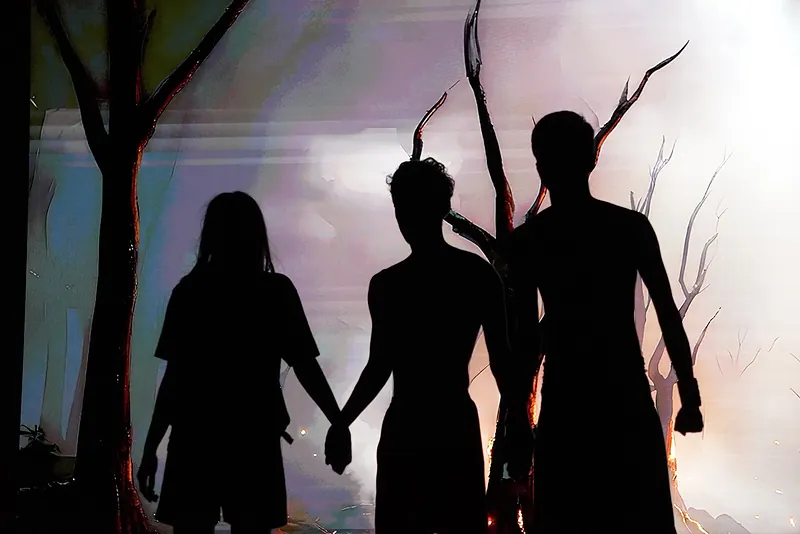 Three figures in silhouette holding hands before bare trees
