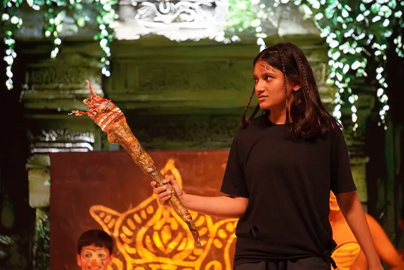A performer in black holding up a flaming torch prop before the temple set
