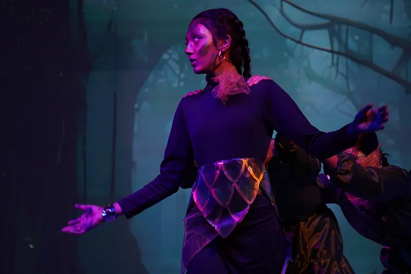 A performer in purple with glowing patterns, arms held out under violet light