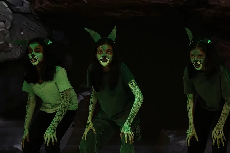 Three actors made up as wolves, crouching in green light