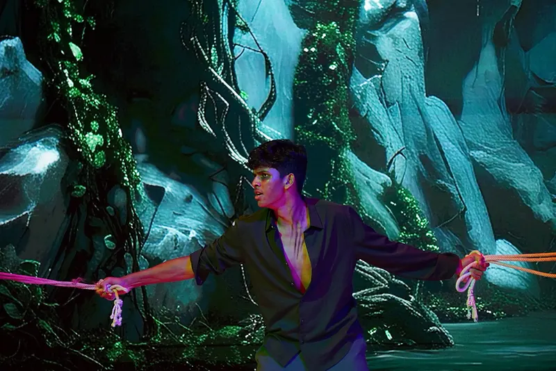 An actor tied with pink rope before a blue cavern backdrop