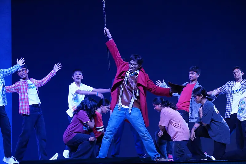 The ensemble dancing under blue light around an actor raising a staff