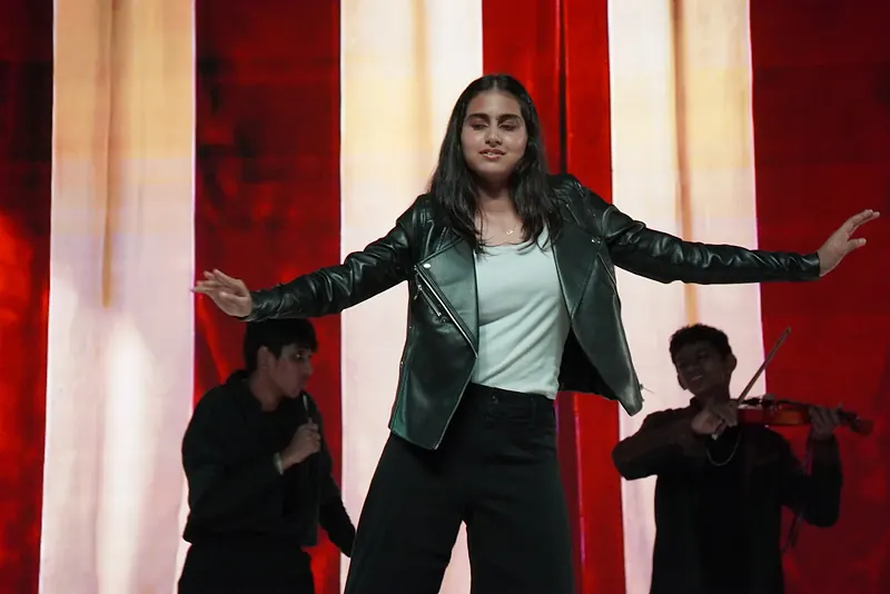 A performer in a leather jacket, arms spread, before striped curtains