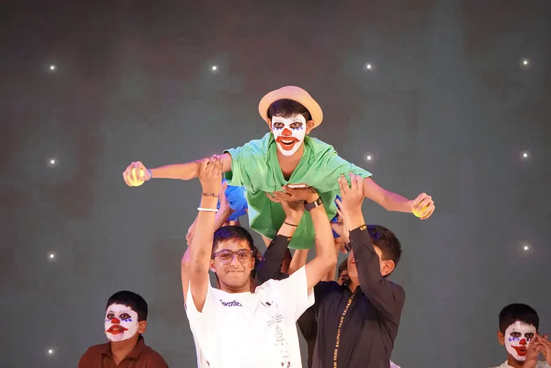 A performer in clown face paint lifted high by others