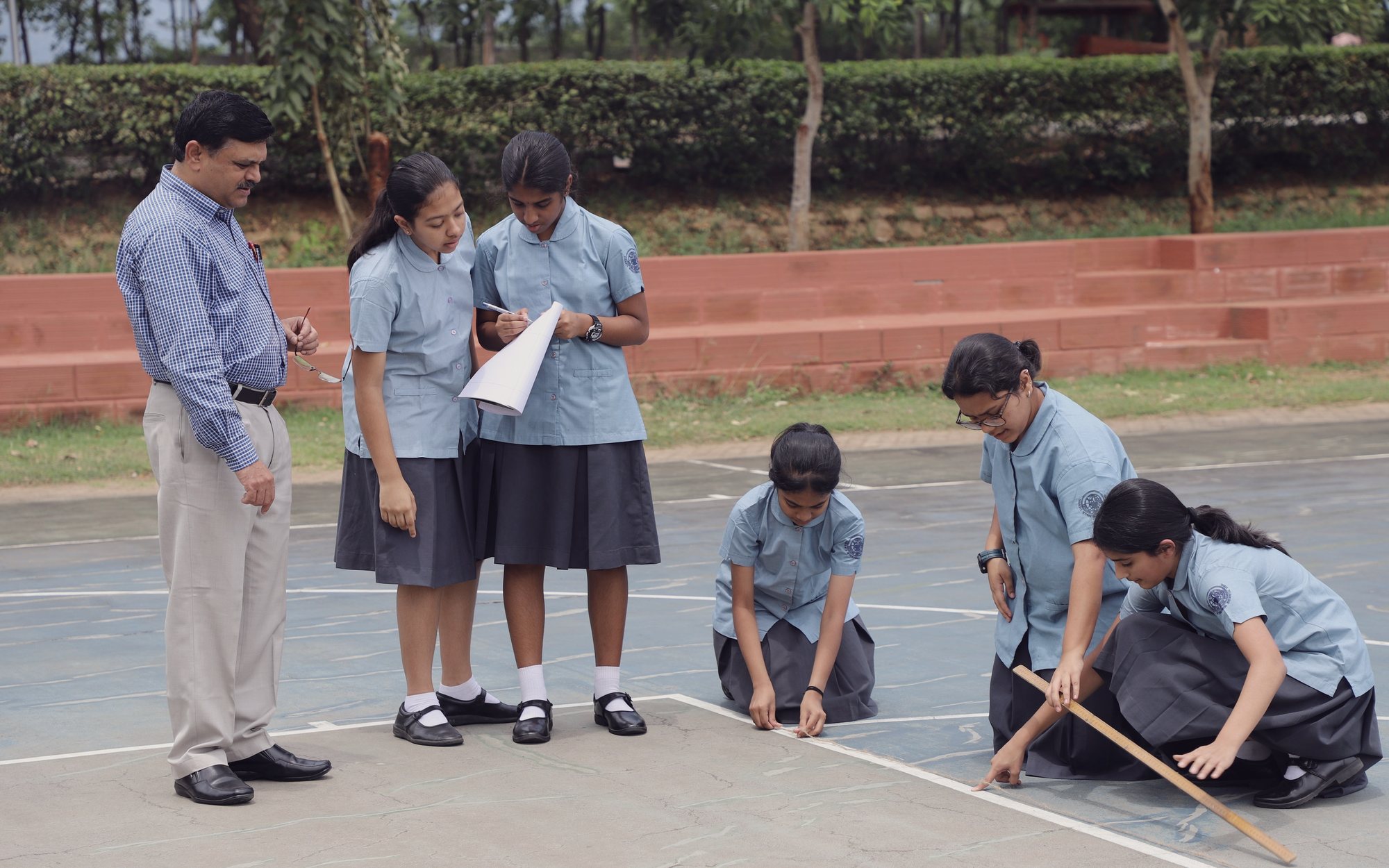 A teacher and five students marking out a court, one of them measuring with a rule